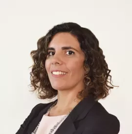Mujer con cabello rizado sonríe, vestida con saco negro.