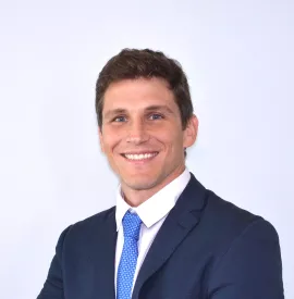 Persona en traje oscuro y corbata azul sonriendo al frente.