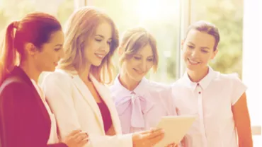 Grupo de mujeres mirando una tableta juntas, sonriendo y conversando.