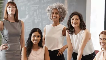 Cinco mujeres posando en una oficina moderna.