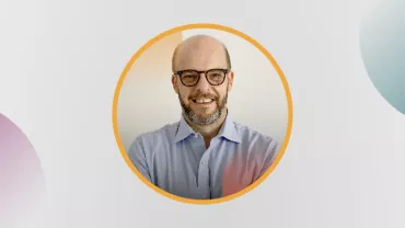 Hombre con camisa azul y gafas sonríe.