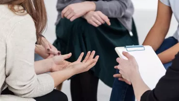 Grupo de personas sentadas, conversando, con un bloc de notas.