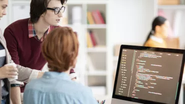 Grupo de jóvenes colaborando frente a una computadora con código.