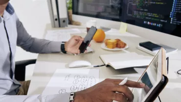 Persona trabajando con una tableta y un ordenador en una oficina.