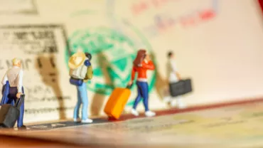 Figuras miniatura con maletas en un pasaporte con sellos.