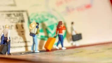 Figuras miniatura con maletas en un pasaporte con sellos.