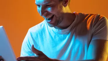 Hombre sonriendo mientras usa una tableta con luz naranja de fondo.