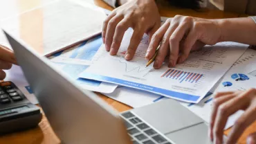 Manos revisando gráficos y documentos financieros en una reunión.