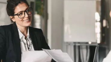 Dos mujeres en una reunión de negocios, una hablando y otra escuchando.