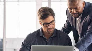 Dos hombres trabajan juntos en una computadora portátil.