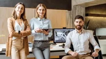 Tres personas en una oficina moderna, sonrientes y vestidas profesionalmente.