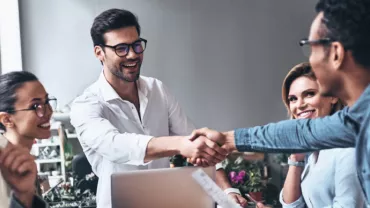 Grupo de personas felices en una reunión, dos hombres dándose la mano.