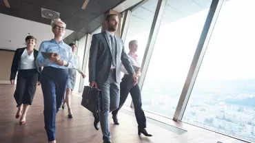 Grupo de personas caminando en un pasillo de oficinas con vista panorámica.