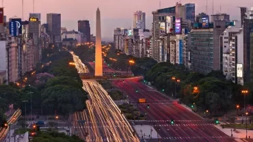 Vista del Obelisco de Buenos Aires al atardecer, rodeado de luces de tráfico.