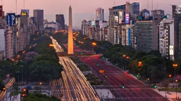 Vista del Obelisco de Buenos Aires al atardecer, rodeado de luces de tráfico.