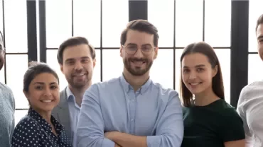 Seis personas sonrientes posando juntas frente a una ventana.