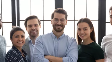 Seis personas sonrientes posando juntas frente a una ventana.