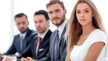 Grupo de personas en una reunión, vestidos de manera formal.