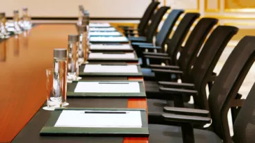 Mesa de conferencias con sillas y cuadernos alineados.