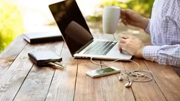 Persona trabajando en un portátil en una mesa al aire libre.