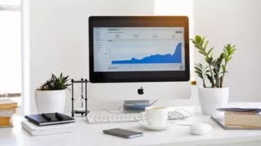 Escritorio blanco con computadora, plantas y gráfica en pantalla.