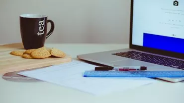 Taza de té y galletas junto a un portátil en un escritorio.