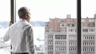 Hombre mirando por la ventana a edificios de la ciudad.