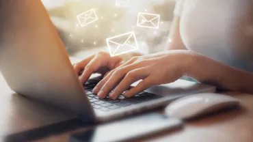 Persona usando una laptop con íconos de correo flotando.