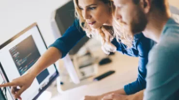 Dos personas trabajando frente a una computadora, revisando código.