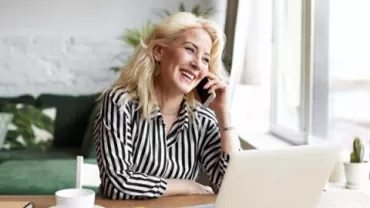Mujer sonriendo mientras habla por teléfono en casa.