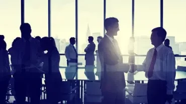 Personas de negocios estrechando manos frente a una ventana en una sala de reuniones.