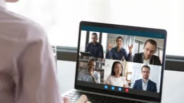 Persona participando en una videollamada con seis colegas en la pantalla de una laptop.