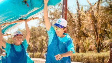 Dos personas con ropa azul cargan un inflable mientras sonríen bajo el sol.