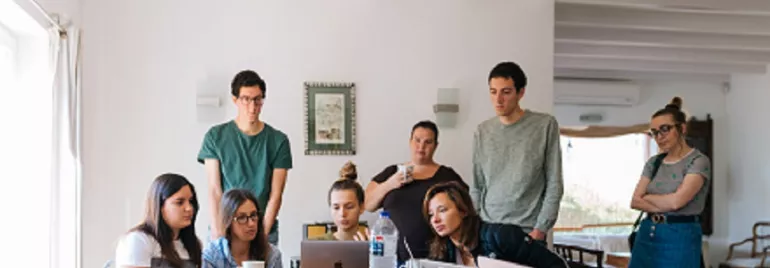 Grupo de personas trabajando en equipo alrededor de una mesa con laptops.