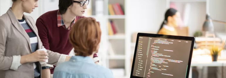 Grupo de jóvenes colaborando frente a una computadora con código.