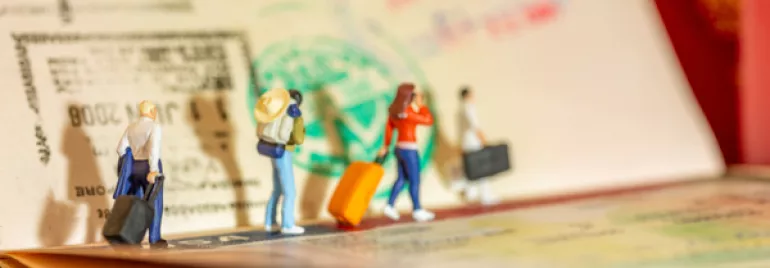 Figuras miniatura con maletas en un pasaporte con sellos.