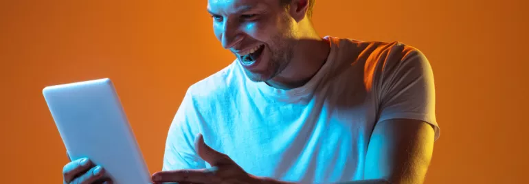 Hombre sonriendo mientras usa una tableta con luz naranja de fondo.