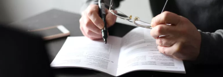 Persona leyendo un documento con gafas y bolígrafo en mano.