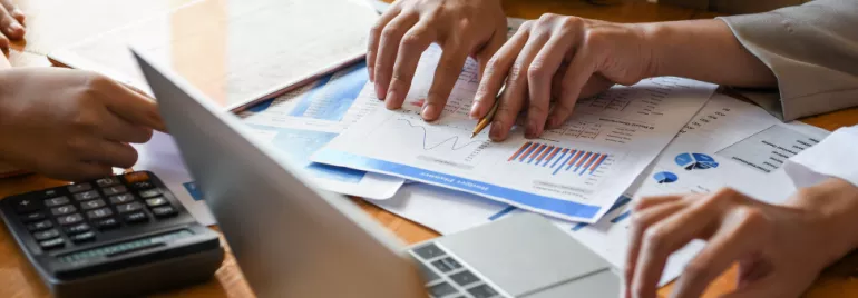 Manos revisando gráficos y documentos financieros en una reunión.
