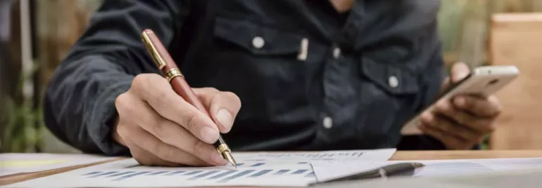 Persona revisando gráficos con un bolígrafo y un teléfono móvil.
