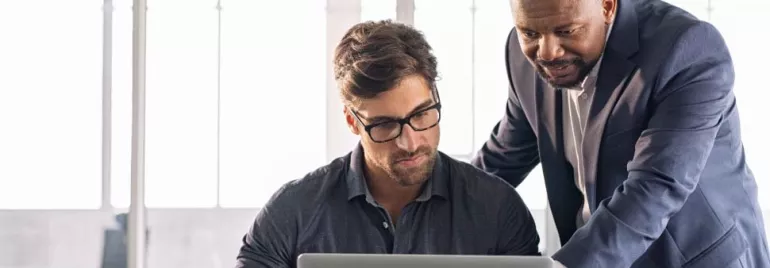 Dos hombres trabajan juntos en una computadora portátil.
