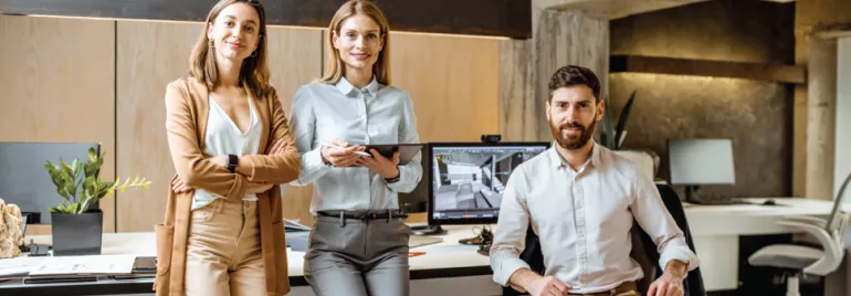 Tres personas en una oficina moderna, sonrientes y vestidas profesionalmente.
