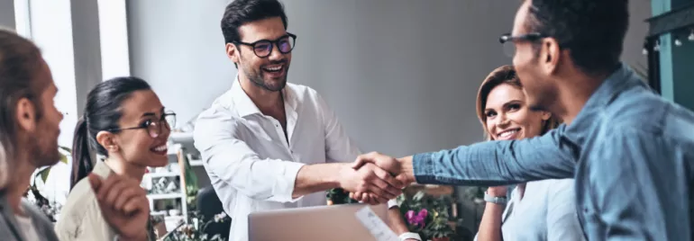 Grupo de personas felices en una reunión, dos hombres dándose la mano.