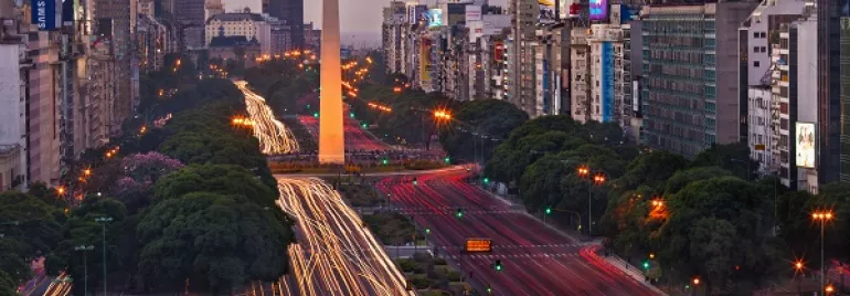Vista del Obelisco de Buenos Aires al atardecer, rodeado de luces de tráfico.
