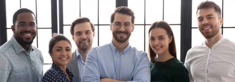 Seis personas sonrientes posando juntas frente a una ventana.