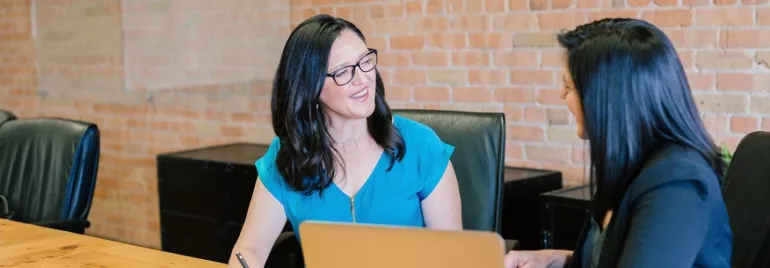 Dos mujeres conversan sonrientes en una sala de reuniones.
