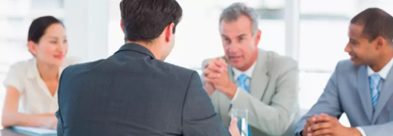 Reunión de negocios con cuatro personas en traje alrededor de una mesa.