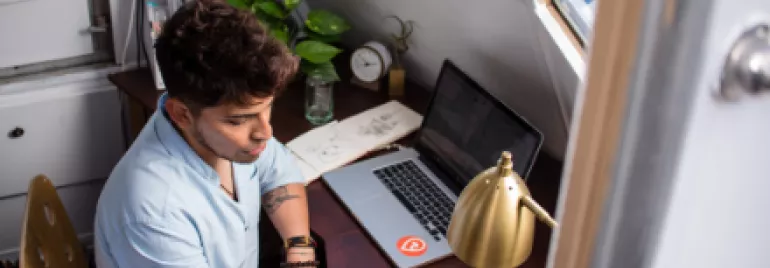 Persona trabajando en un escritorio con laptop y bloc de notas.