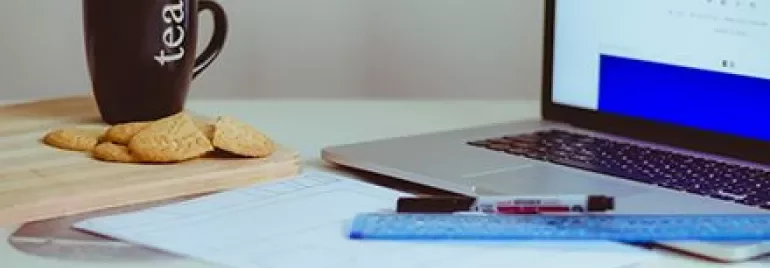 Taza de té y galletas junto a un portátil en un escritorio.
