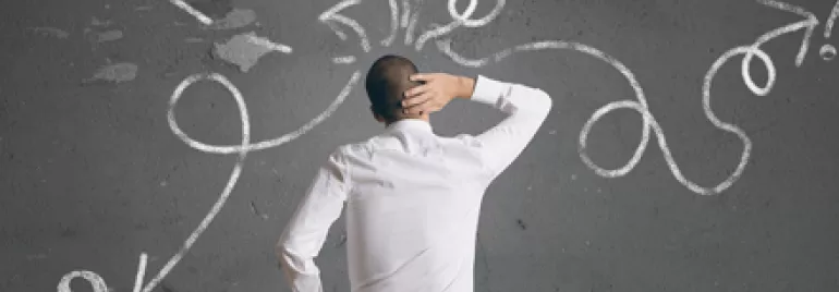 Persona pensativa ante una pizarra con signos de interrogación y flechas.